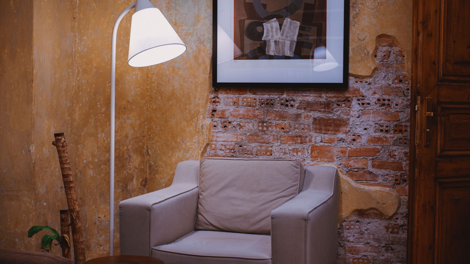 Leesfauteuil en staande lamp voor een wand met kalkafwerking en baksteen
