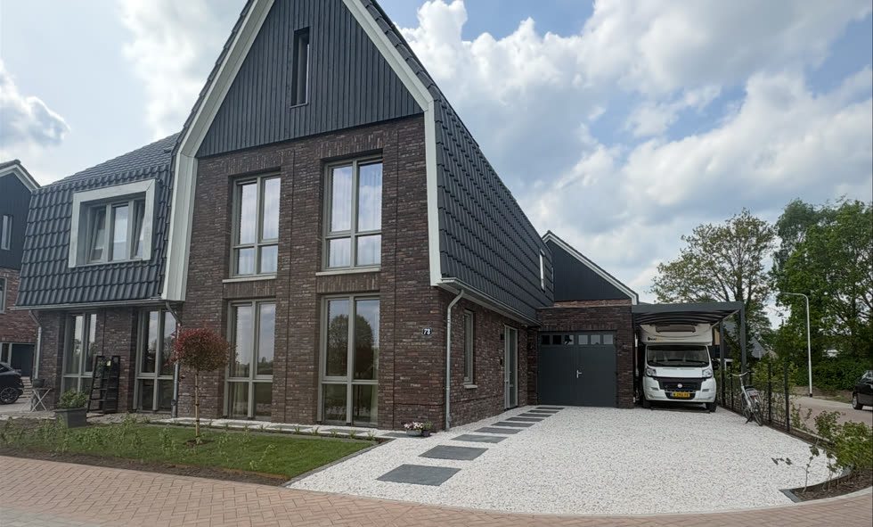 Bakstenen woning met donkere gevelbekleding en een grindoprit