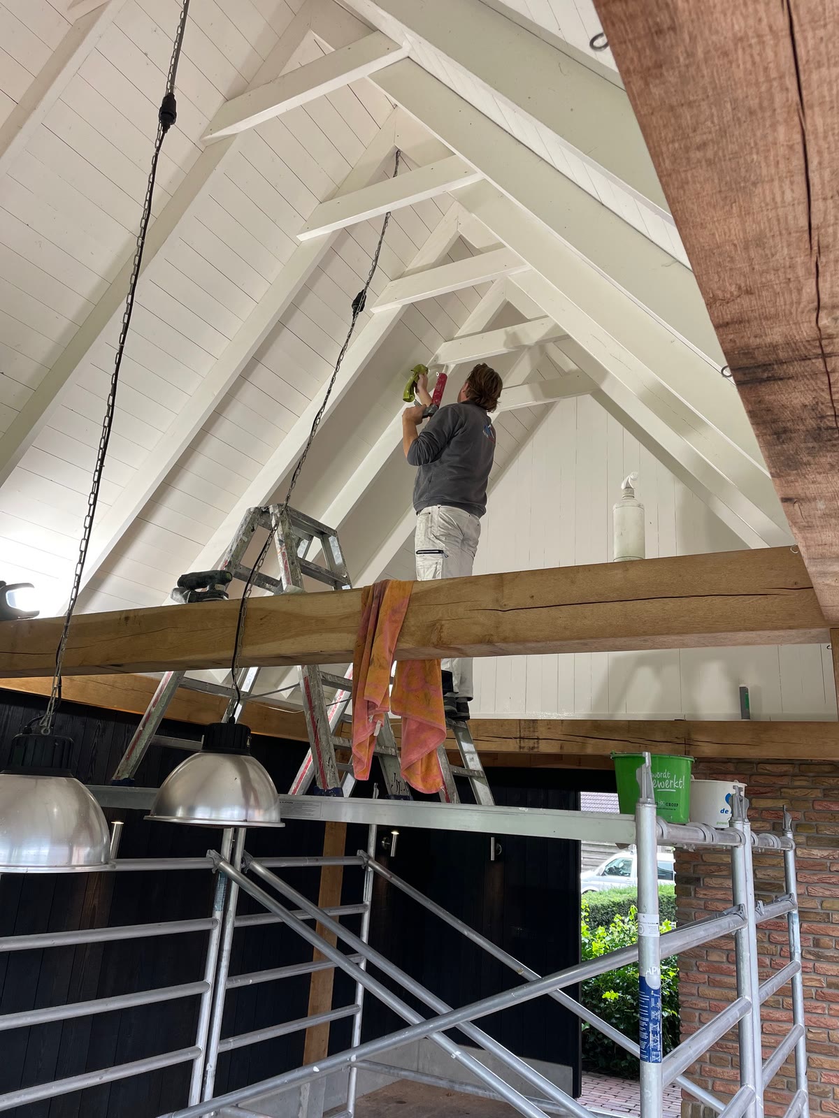 Schilder aan het werk vanaf een rolsteiger, onder een houten kap met witte balken