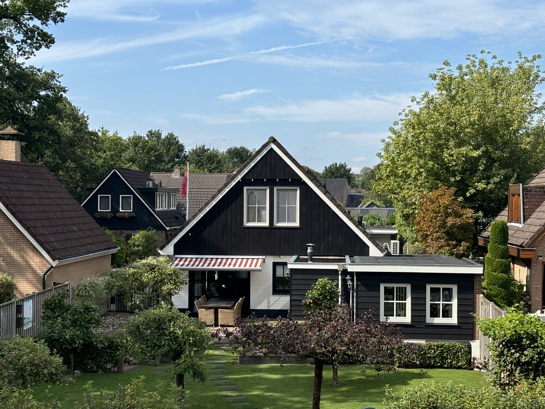 Zwart geschilderde houten woning met witte kozijnen in een groene tuin